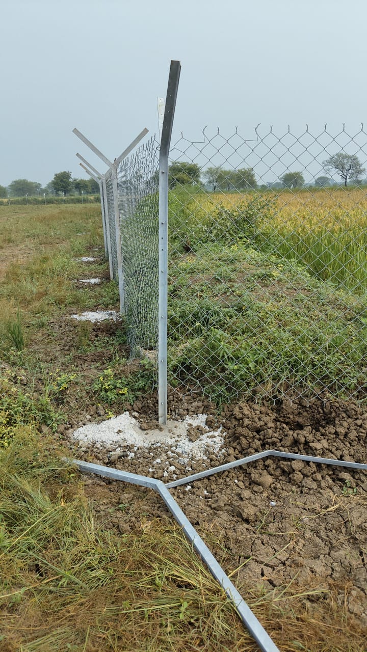 Chain-link boundary fence post grouted into a concrete base at the site edge